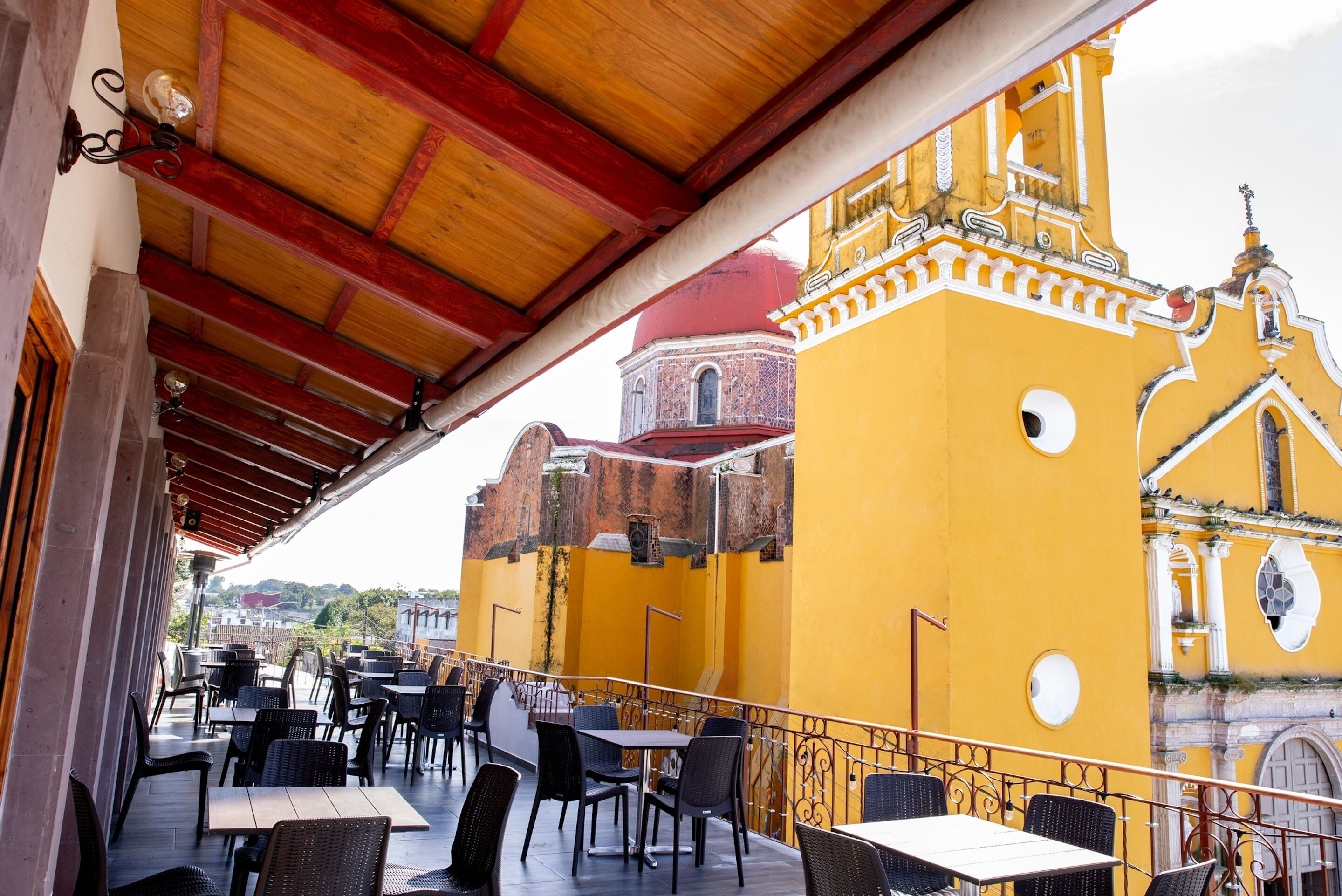 Eine Außenpatio mit Tischen und Stühlen, mit Blick auf ein gelbes Gebäude mit einer roten Kuppel und aufwendiger Architektur.