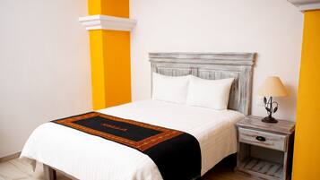 A neatly made bed with a white and black bedspread, a wooden nightstand with a lamp, and a yellow accent wall.