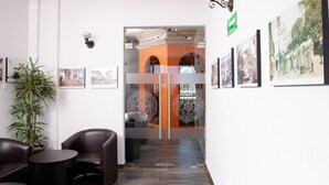 Un vestíbulo con techo de madera, una planta en maceta, sillones de cuero, una mesita y fotografías enmarcadas en las paredes.
