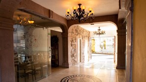 Vestíbulo de hotel con candelabro, piso estampado y puerta de vidrio con el nombre del hotel.