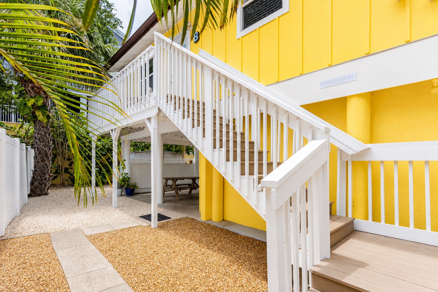A yellow building with a white staircase and a covered outdoor area with a bench.