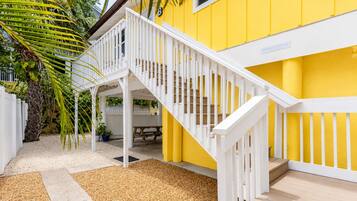 A yellow building with a white staircase and a covered outdoor area with a bench.