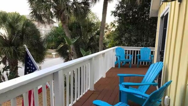 A wooden deck with blue chairs and a white railing, overlooking palm trees and a building. - Indian Rocks Gem: Walk to Beach and Dining from Cozy retreat! (Indian Rocks Beach)