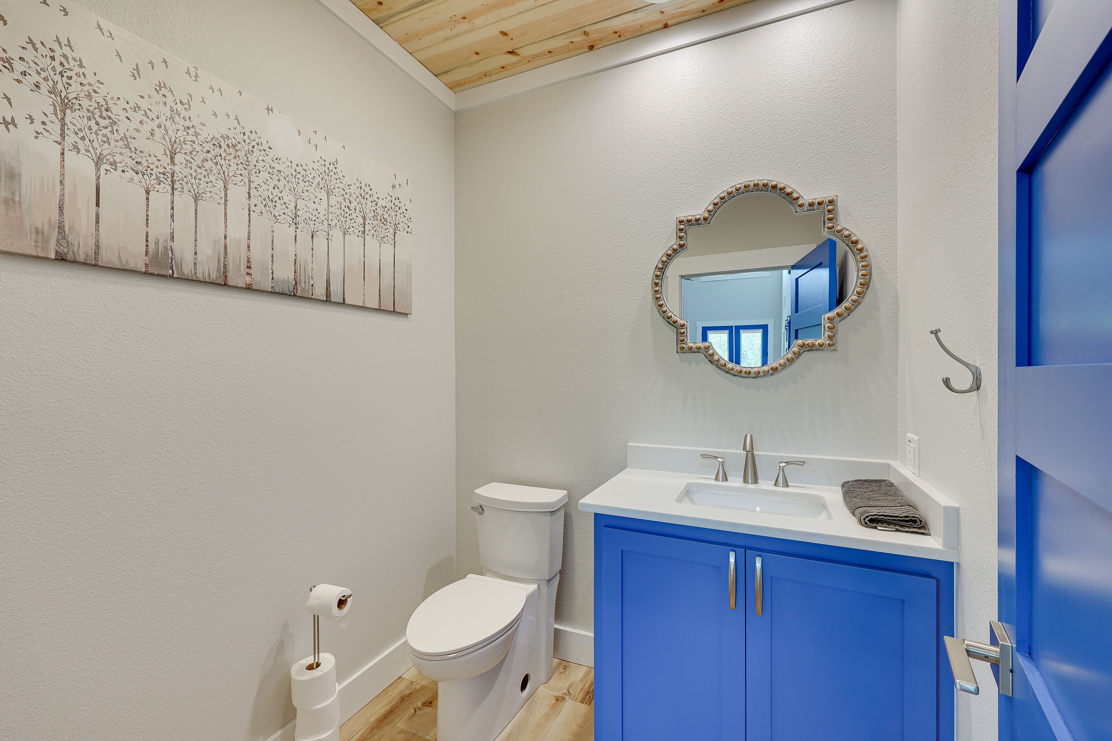 A bathroom with a white toilet, a blue cabinet, a sink, and a mirror with lights.
