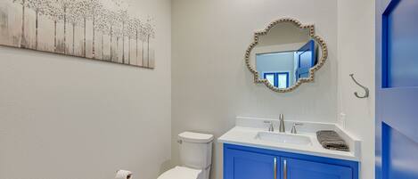 A bathroom with a white toilet, a blue cabinet, a sink, and a mirror with lights.