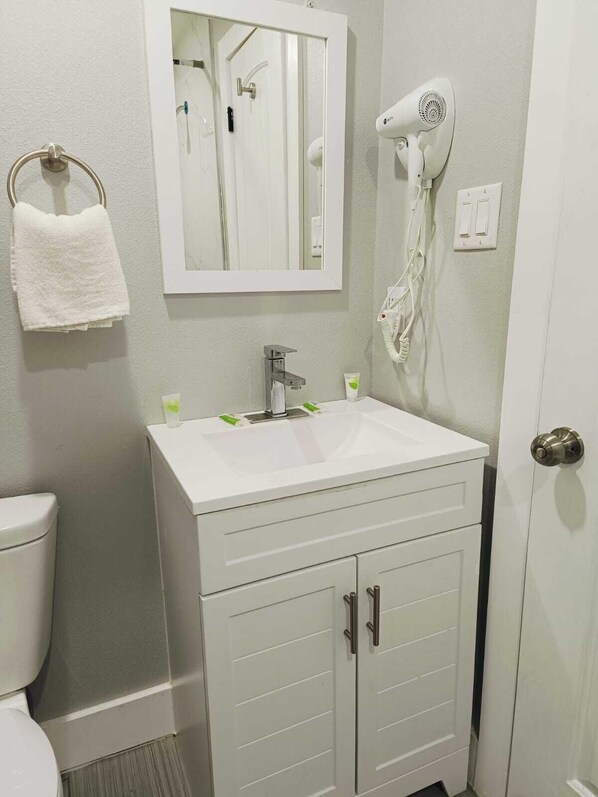 A bathroom with a white sink, a mirror, a towel rack, a hairdryer, and a toilet.
