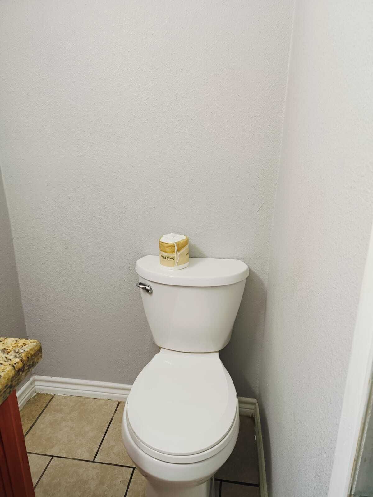 A white toilet with a toilet paper box on top, located in a bathroom with white walls and tiled floor.