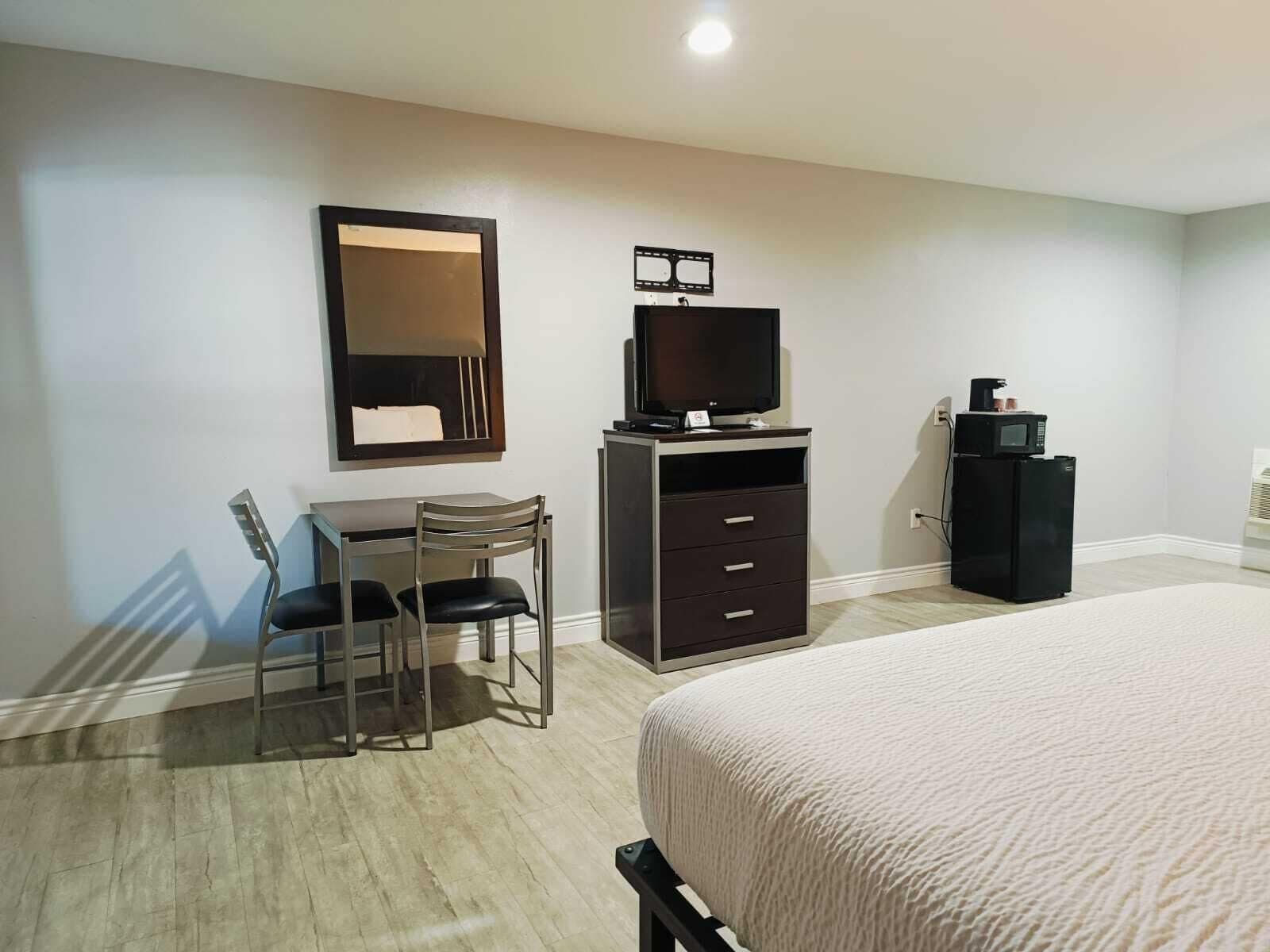A hotel room with a bed, a desk with a chair, a TV, a dresser, and a microwave.