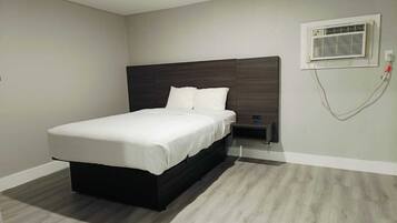 A modern bedroom with a large bed, a nightstand, a wall-mounted air conditioning unit, and a light switch.