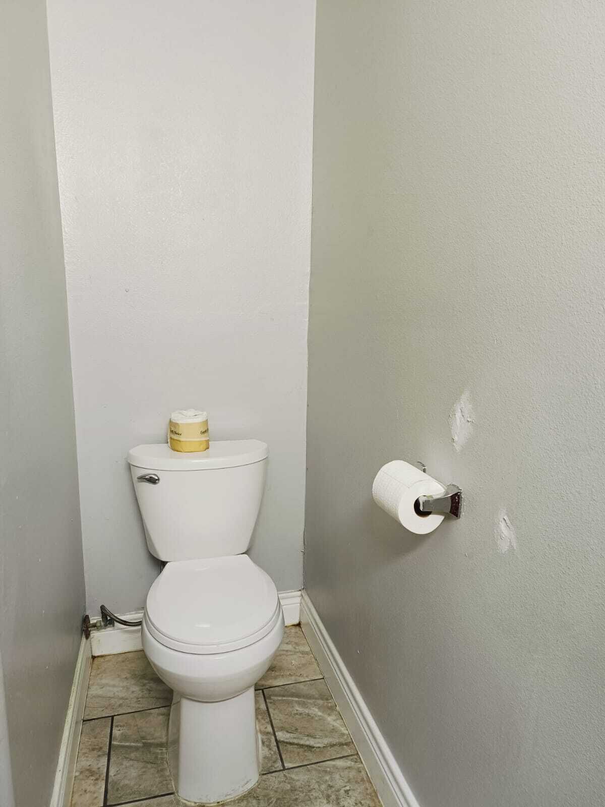Une petite salle de bain avec des toilettes, un rouleau de papier toilette et un mur partiellement peint.