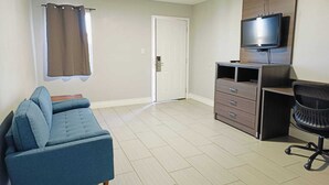 A room with a blue sofa, a TV on a wooden cabinet, a door, and a window with curtains. - Village Inn Motel (Rockport)
