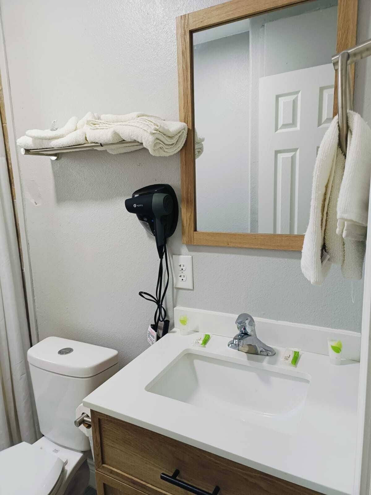 A bathroom with a white sink, a mirror, a towel rack, and a hairdryer on the wall.
