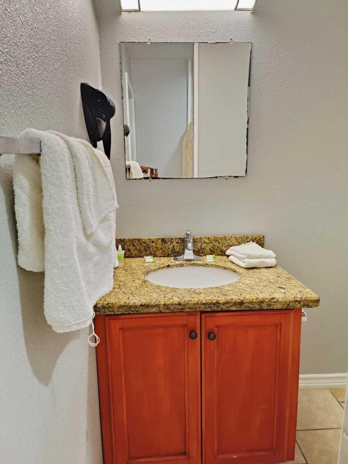 A bathroom with a granite countertop sink, a mirror above it, and a towel rack with a white towel hanging.