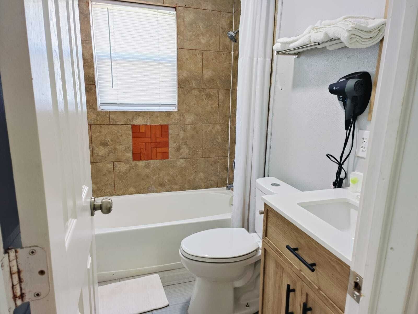 Casa de banho com banheira, sanita e secador de cabelo sobre a bancada.