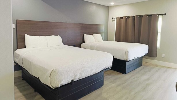 A hotel room with two beds, a wooden headboard, a window with curtains, and a light-colored floor. - Village Inn Motel (Rockport)