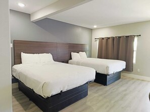 A hotel room with two beds, a wooden headboard, a window with curtains, and a light-colored floor.