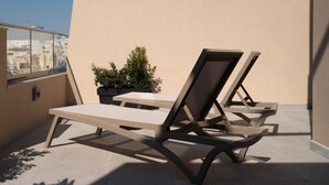 A rooftop terrace with two lounge chairs and a potted plant. - Portside Lodge Building (Marsaskala)