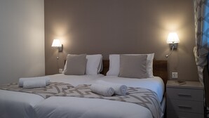 A double bed with two pillows, a bedside table with a lamp, and a folded towel on the bed. - Portside Lodge Building (Marsaskala)