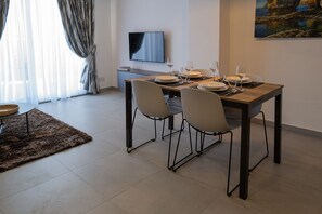 Un comedor con una mesa lista para cuatro, un televisor de pantalla plana en la pared y un cuadro de una escena costera.