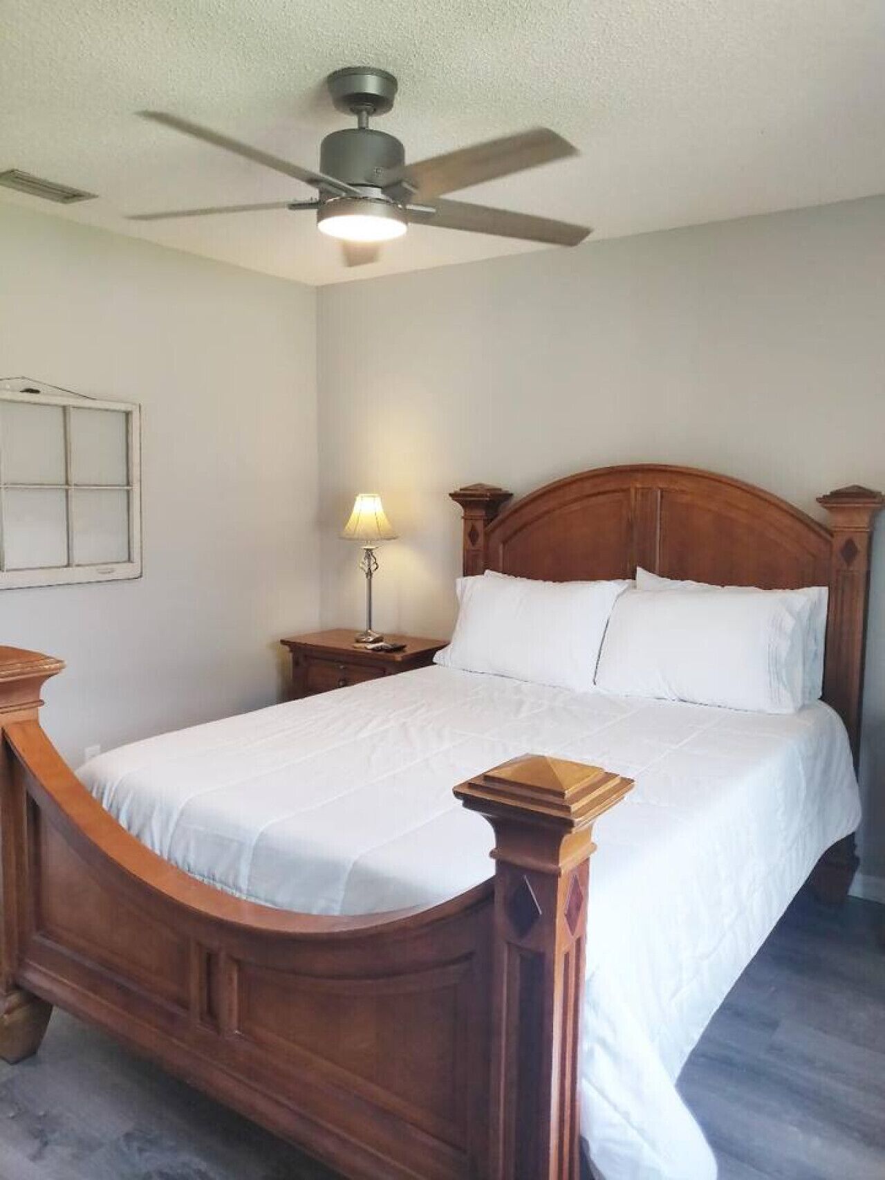 A bedroom with a wooden bed, a nightstand, a lamp, and a ceiling fan.