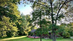 A well-maintained lawn with a wooden deck, a tree, and a rustic cabin in the background. - Log Home w/ Shared Beach and Game Room. (Walker)