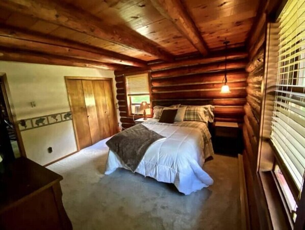 A log cabin bedroom with a bed, a dresser, and a window with blinds.