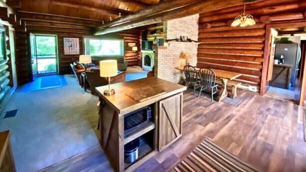 A log cabin interior with a central dining area, a fireplace, and a kitchen area. - Log Home w/ Shared Beach and Game Room. (Walker)