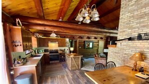 A rustic kitchen with wooden cabinets, a central island, and a dining area with a wooden table and chairs. - Log Home w/ Shared Beach and Game Room. (Walker)