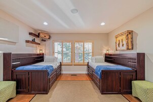 Una habitación con dos camas de madera, un ventanal con persianas, techo de madera y una alfombra pequeña en el suelo.