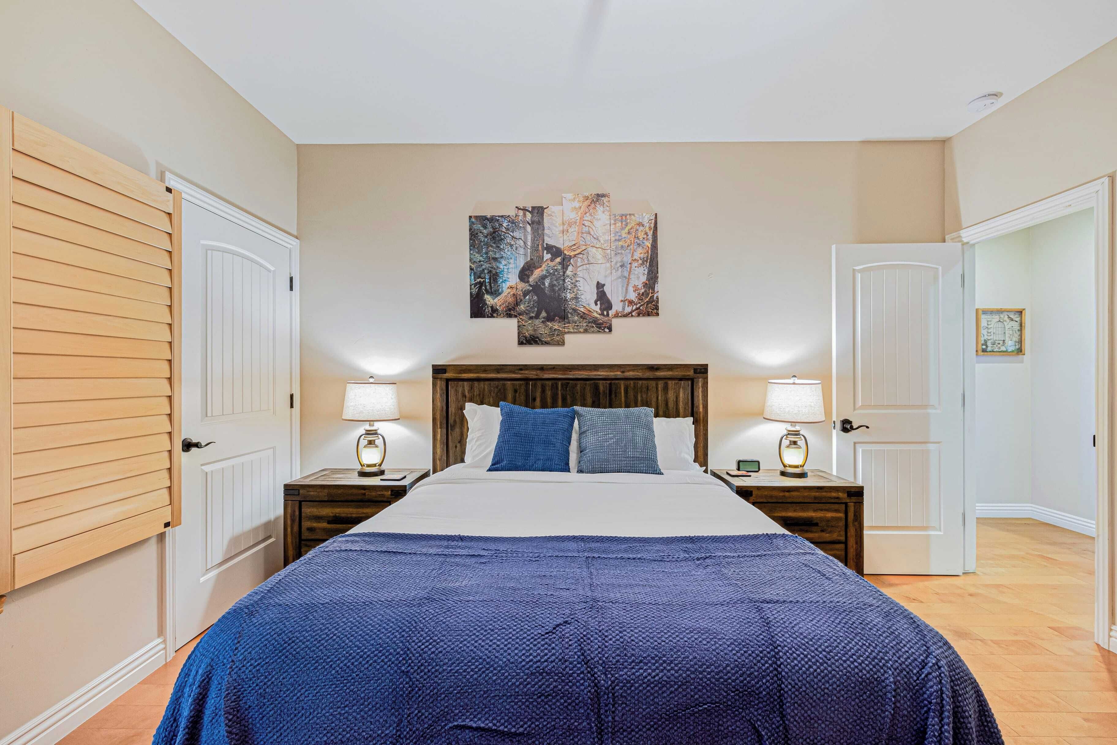 A bedroom with a large bed, two bedside tables with lamps, a wooden headboard, and a wall-mounted artwork.