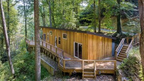 Une cabane en bois dotée d’une terrasse et d’un escalier, entourée d’arbres.