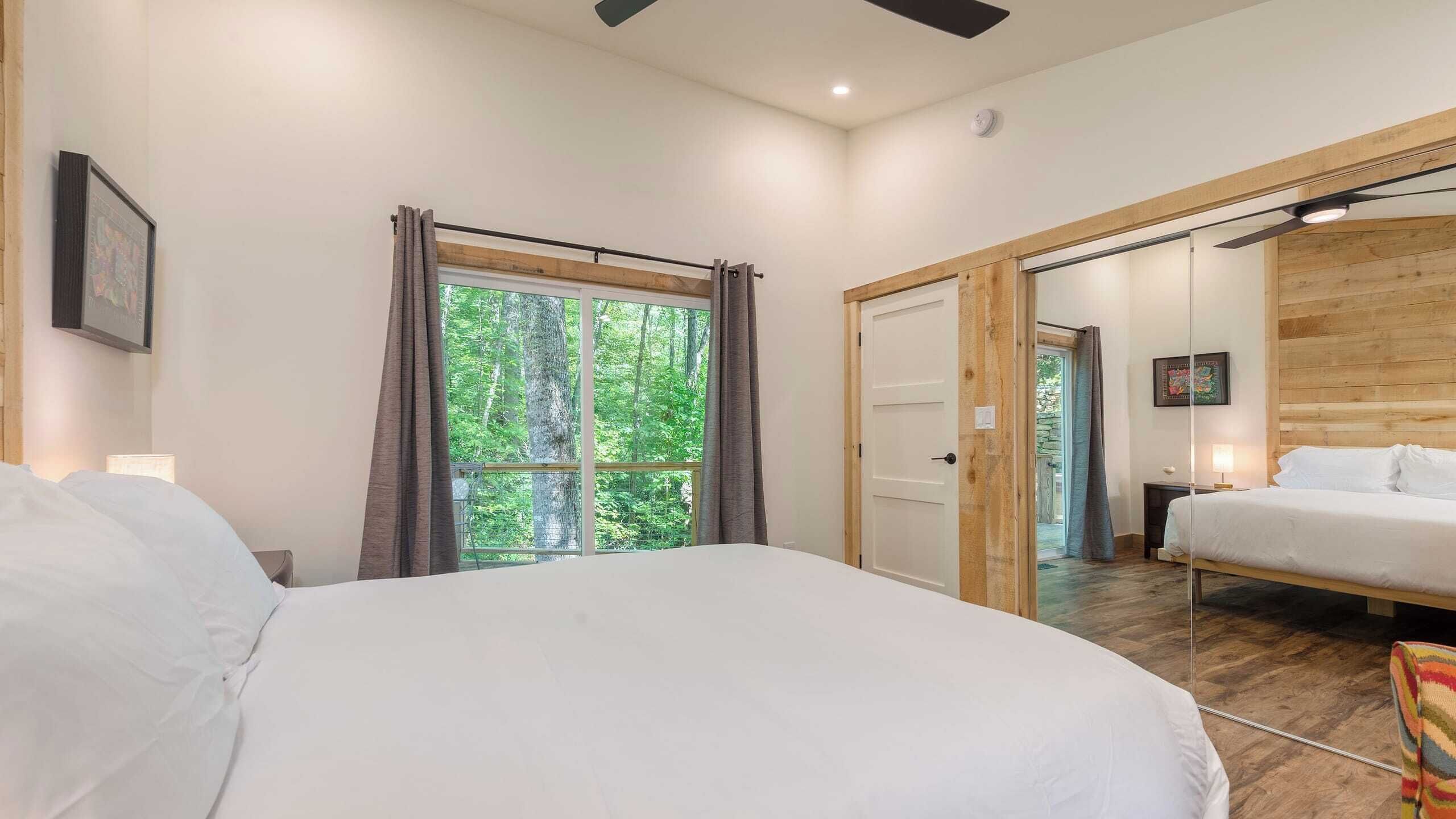Un dormitorio con una cama grande, una ventana con cortinas, una puerta que da a otra habitación y un cabecero de madera.
