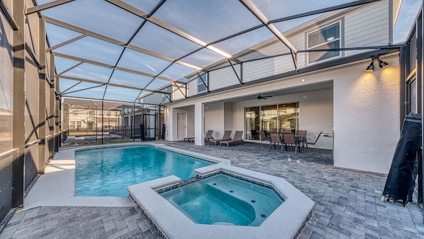 A covered outdoor swimming pool with lounge chairs and a hot tub.