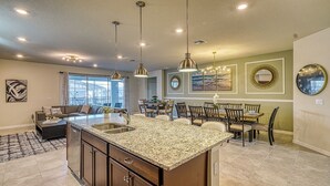 A spacious kitchen with granite countertops, pendant lighting, and a dining area with wooden chairs. - Luxury 8BR Retreat | Private Pool, Spa & Resort Amenities | Near Disney (Davenport)