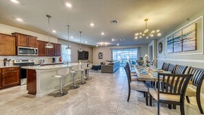 A spacious kitchen with a central island, bar stools, and a dining area with a long table and chairs. - Luxury 8BR Retreat | Private Pool, Spa & Resort Amenities | Near Disney (Davenport)