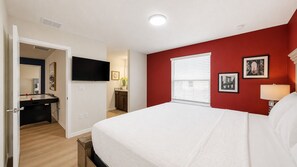 A bedroom with a bed, a desk, a TV, a window with blinds, and a wall with framed pictures. - Luxury 8BR Retreat | Private Pool, Spa & Resort Amenities | Near Disney (Davenport)