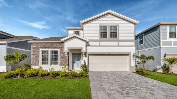 A two-story house with a garage, a front lawn, and a brick driveway. - Luxury 8BR Retreat | Private Pool, Spa & Resort Amenities | Near Disney (Davenport)