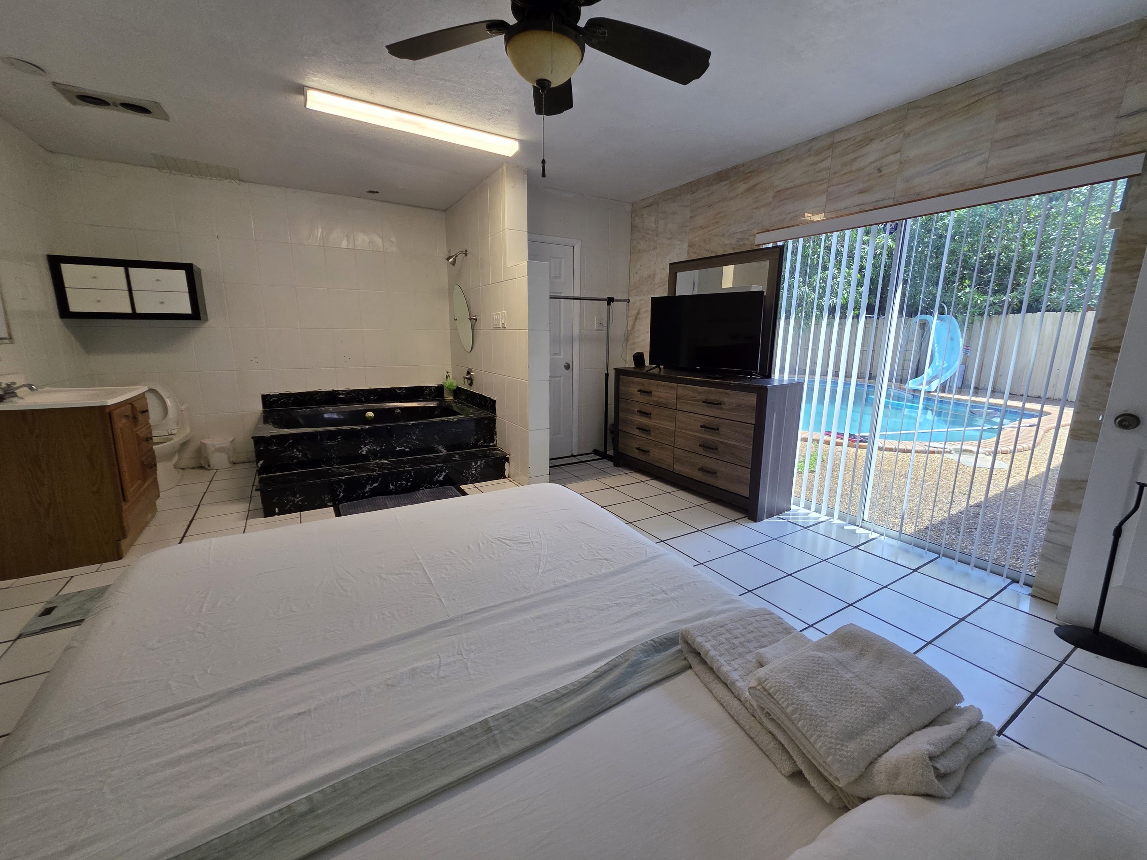 A bedroom with a bed, a dresser, a TV, and a sliding glass door leading to a pool area.