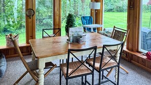 A wooden dining table with six chairs, a blue chair, and a small table with a lamp.