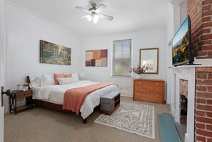 A bedroom with a bed, a dresser, a television, and a fireplace. - Redstick Cottage (Baton Rouge)