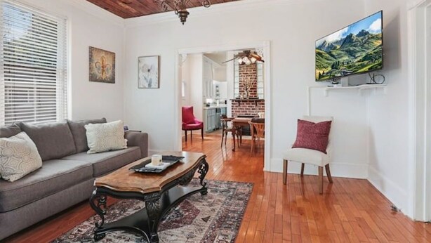 A living room with a sofa, coffee table, and a TV mounted on the wall. - Redstick Cottage (Baton Rouge)