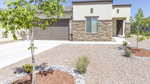 Une maison moderne à deux étages, dotée d’une façade en pierre, d’un garage et d’un jardin aménagé avec de petits arbustes et un arbre.