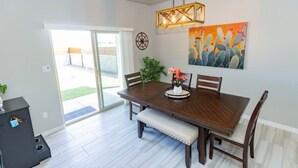 Un coin repas avec une table en bois, des chaises et un banc. Un luminaire suspendu se trouve au-dessus de la table et un tableau est accroché au mur.