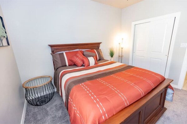 A bedroom with a wooden bed, a grey carpet, a black wire basket, and a white door. - Modern Farmhouse Near Bike Path with Spectacular Views! (Las Cruces)
