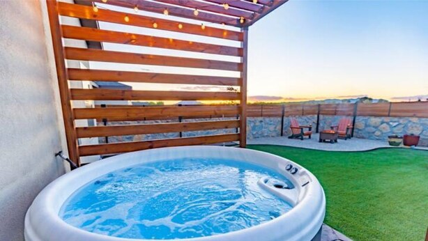 Un bain à remous dans un jardin, surmonté d’une pergola en bois et avec un mur de pierres en arrière-plan.