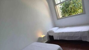 A room with two single beds, a window with a view of greenery, and a small table with a lamp.