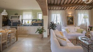 A spacious living area with a kitchen in the background, wooden ceiling beams, and a white sofa. - Villa Trevinano - Private villa with pool in Lazio (Acquapendente)