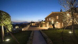 A well-lit pathway leading to a stone building with multiple windows, surrounded by a manicured lawn and trees. - Villa Trevinano - Private villa with pool in Lazio (Acquapendente)