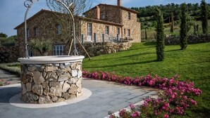 A stone house with a stone fountain in the foreground, surrounded by a well-maintained lawn and flowering plants. - Villa Trevinano - Private villa with pool in Lazio (Acquapendente)