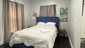 A bedroom with a bed, curtains, a nightstand, and wall art.